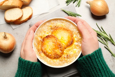 Photo of Woman with bowl of tasty homemade french onion soup at grey table, top view