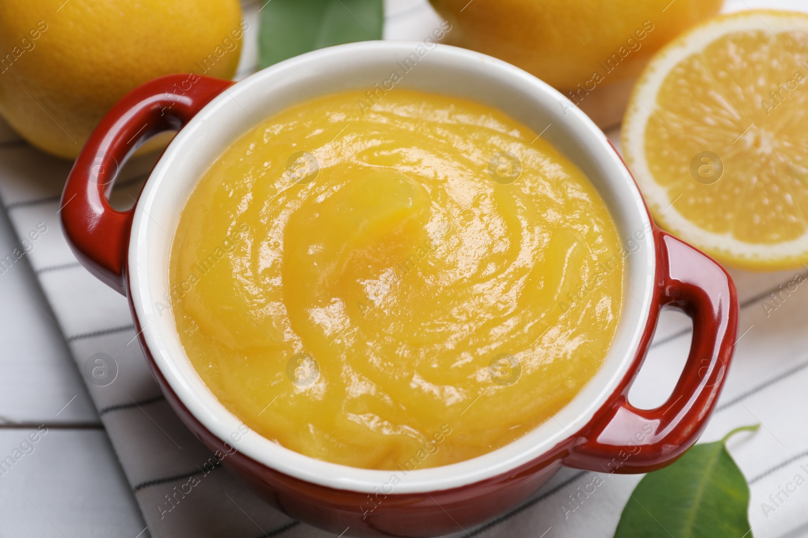 Photo of Delicious lemon curd in bowl and fresh citrus fruits on table, closeup