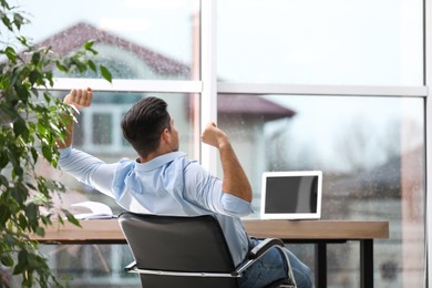 Businessman relaxing in office chair at workplace, back view. Space for text