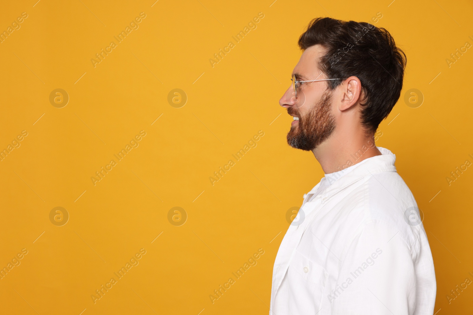 Photo of Profile portrait of smiling bearded man with glasses on orange background. Space for text