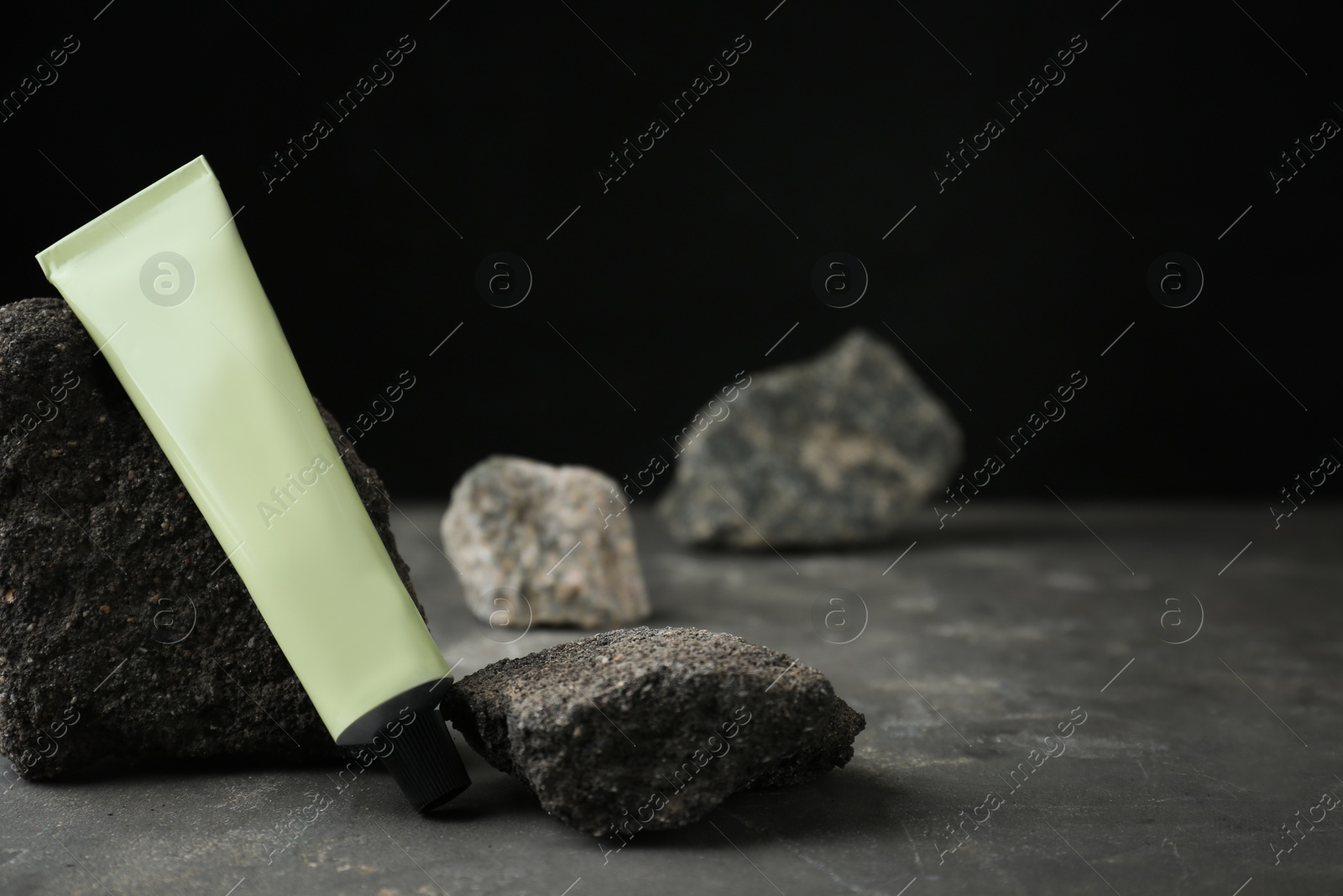 Photo of Tube of hand cream among stones on grey table against dark background. Mockup for design