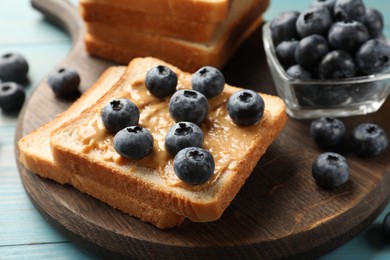 Photo of Delicious toasts with peanut butter and blueberries on light blue wooden table, closeup