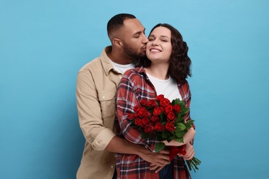 Happy couple celebrating Valentine's day. Beloved woman with bouquet of red roses on light blue background