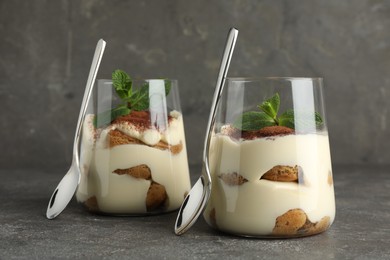 Photo of Delicious tiramisu with mint in glasses on grey table