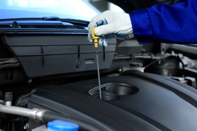 Photo of Worker checking motor oil level in car with dipstick, closeup