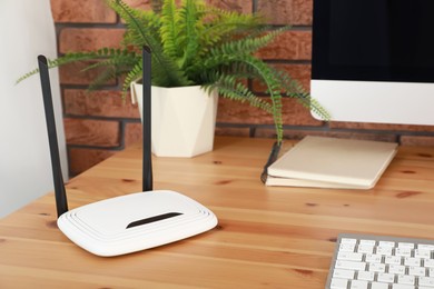 Modern wi-fi router near computer on wooden table