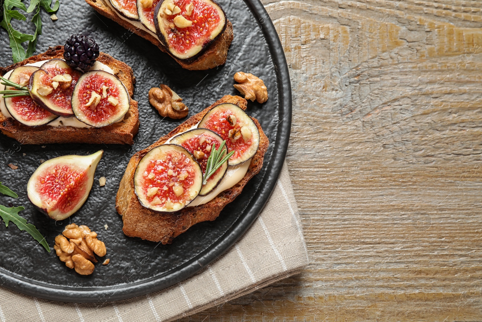 Photo of Bruschettas with cream cheese and figs served on wooden table, top view. Space for text