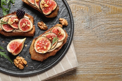 Photo of Bruschettas with cream cheese and figs served on wooden table, top view. Space for text