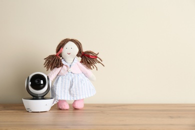 Photo of Baby monitor and toy on wooden table, space for text. CCTV equipment
