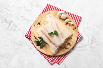 Photo of Pieces of raw cod fish, spices, garlic and parsley on white marble table, top view