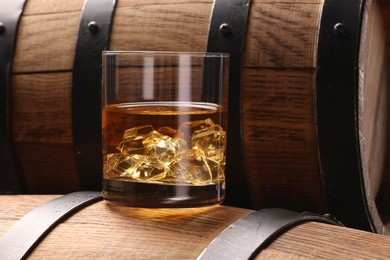 Whiskey with ice cubes in glass on wooden barrel, closeup