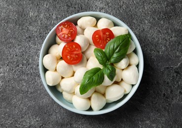 Delicious mozzarella balls, tomatoes and basil leaves in bowl on light gray textured table, top view