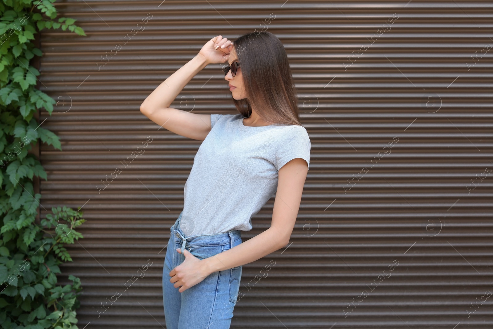 Photo of Young woman wearing gray t-shirt near wall on street. Urban style