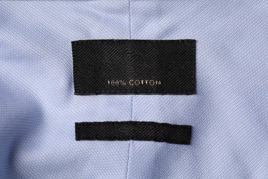 Photo of Empty clothing label on light blue garment, top view