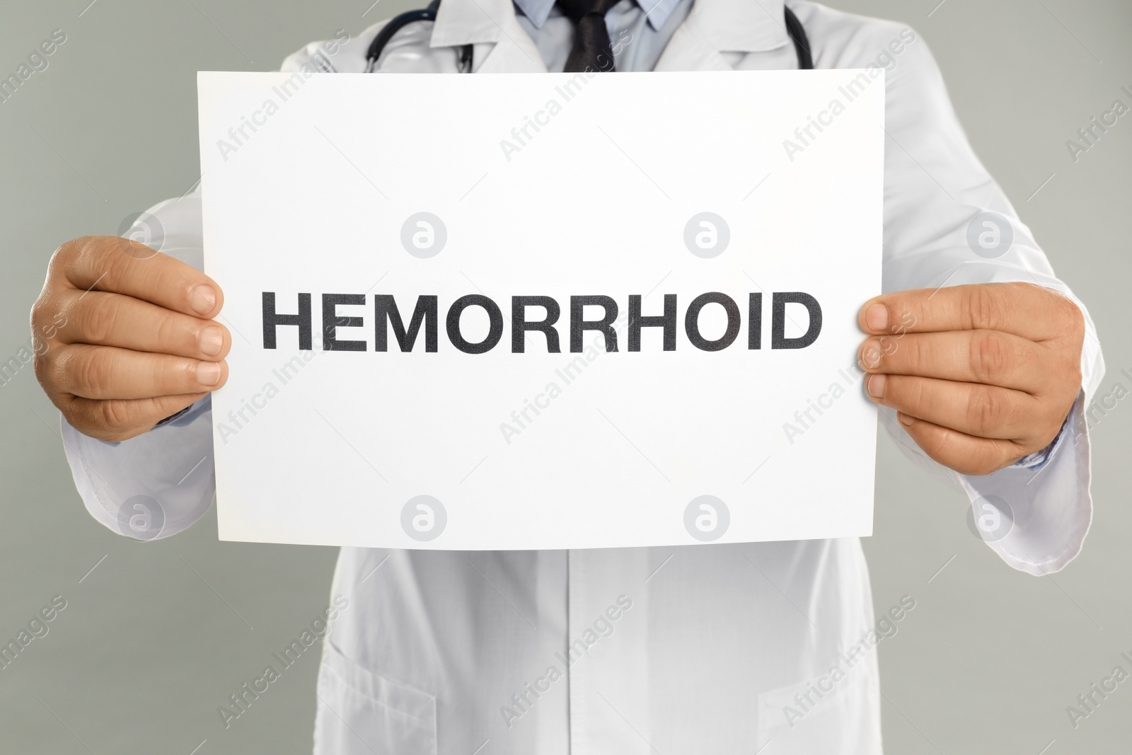 Photo of Doctor holding sign with word HEMORRHOID on light grey background, closeup