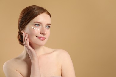 Photo of Beautiful woman with freckles and cream on her face against beige background. Space for text