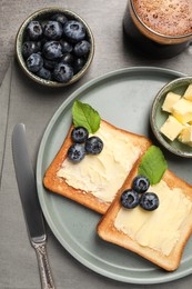 Photo of Delicious toasts served with butter, blueberries and coffee on grey wooden table, flat lay
