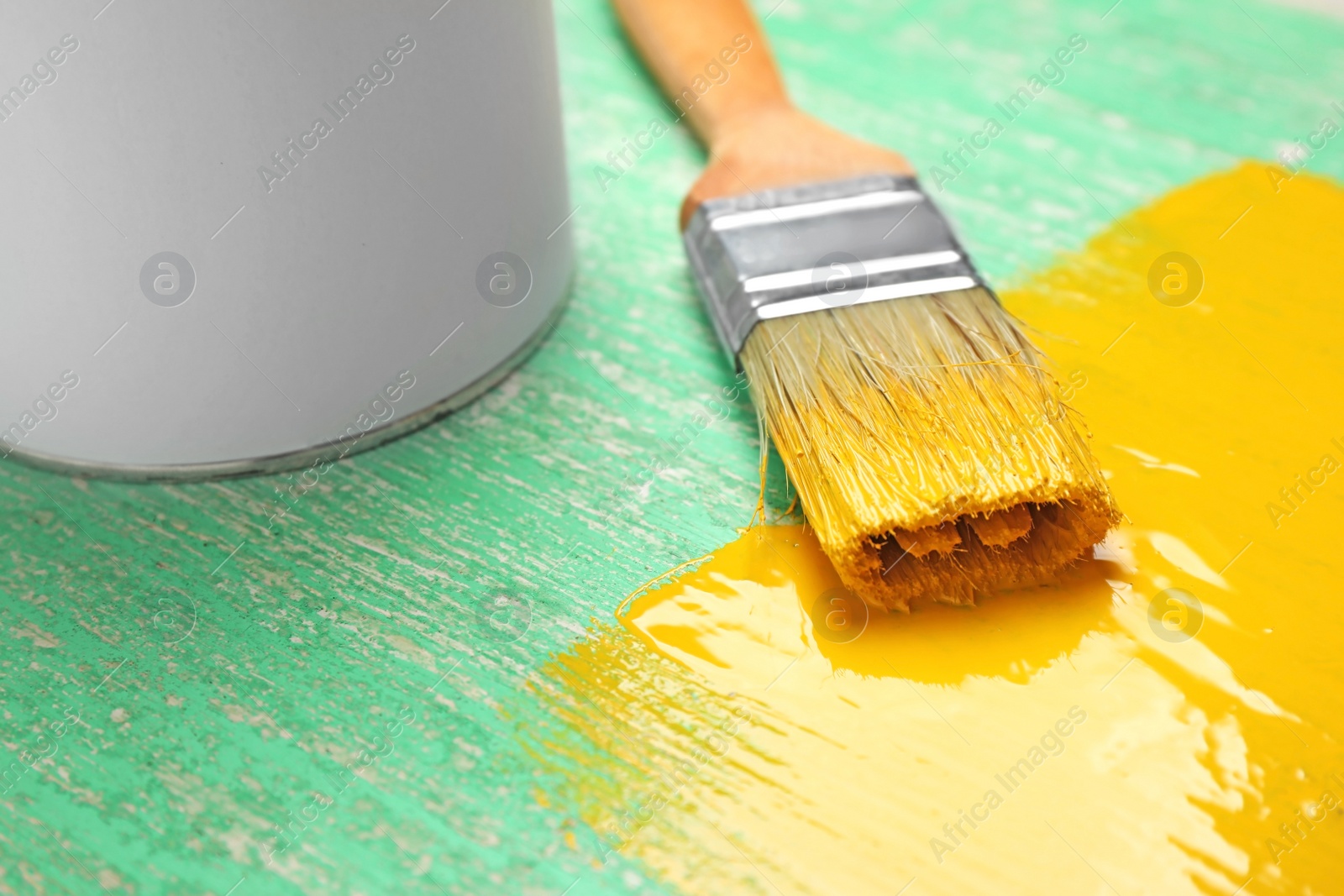 Photo of Brush with yellow paint on green wooden background, closeup