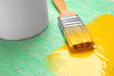 Brush with yellow paint on green wooden background, closeup