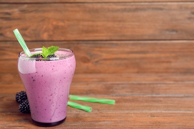 Glass of blackberry smoothie and straws on wooden table. Space for text