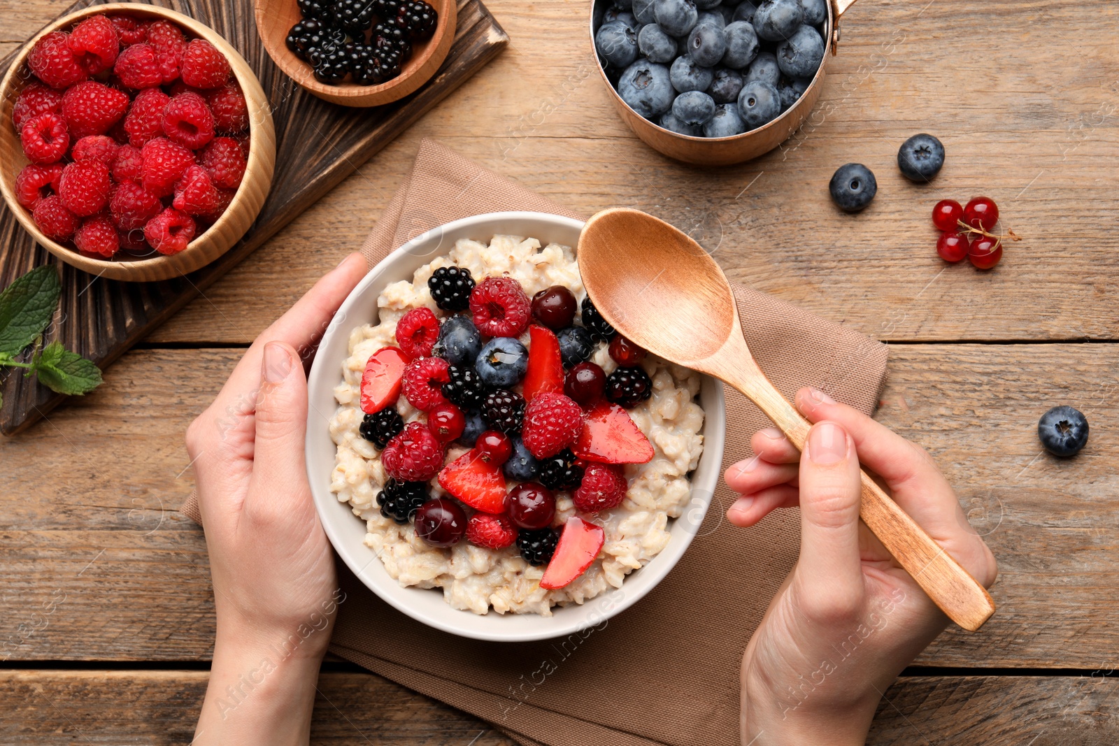 Photo of Woman eating tasty oatmeal porridge at wooden table, top view. Healthy meal