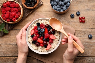 Photo of Woman eating tasty oatmeal porridge at wooden table, top view. Healthy meal