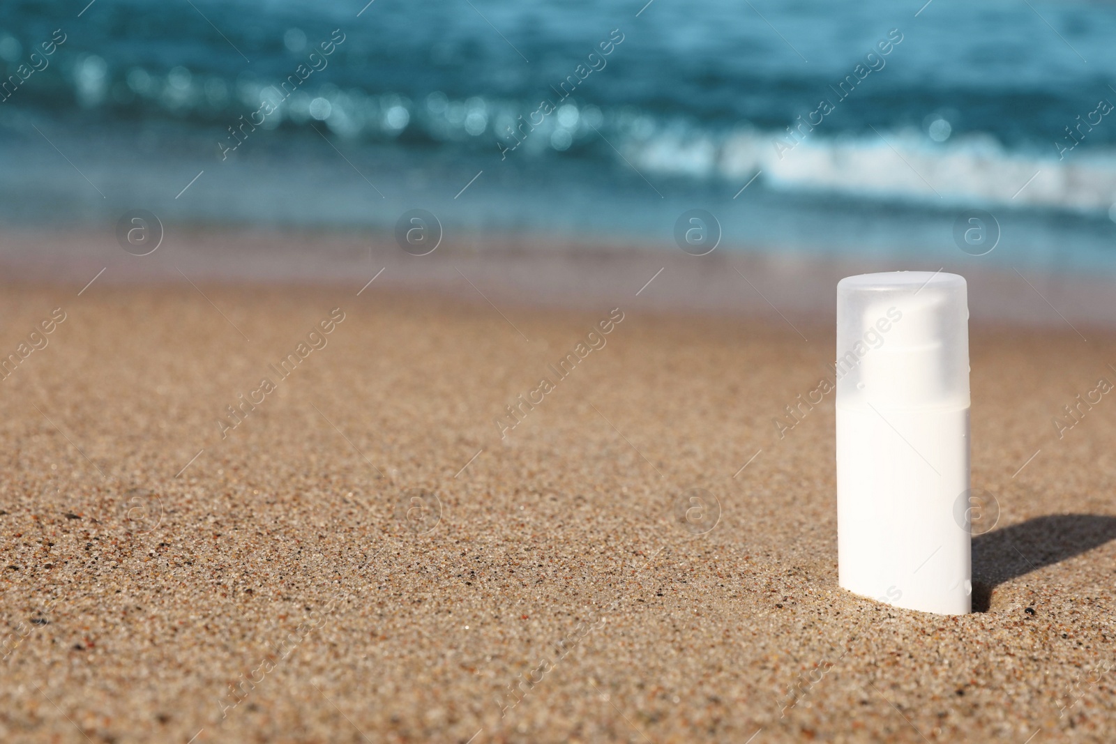 Photo of Blank white bottle of sunscreen on sand near sea, space for text