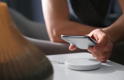 Photo of Man putting smartphone on wireless charger in room, closeup