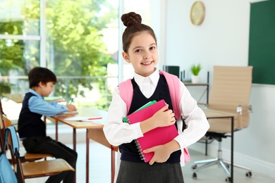 Girl wearing school uniform with backpack in classroom