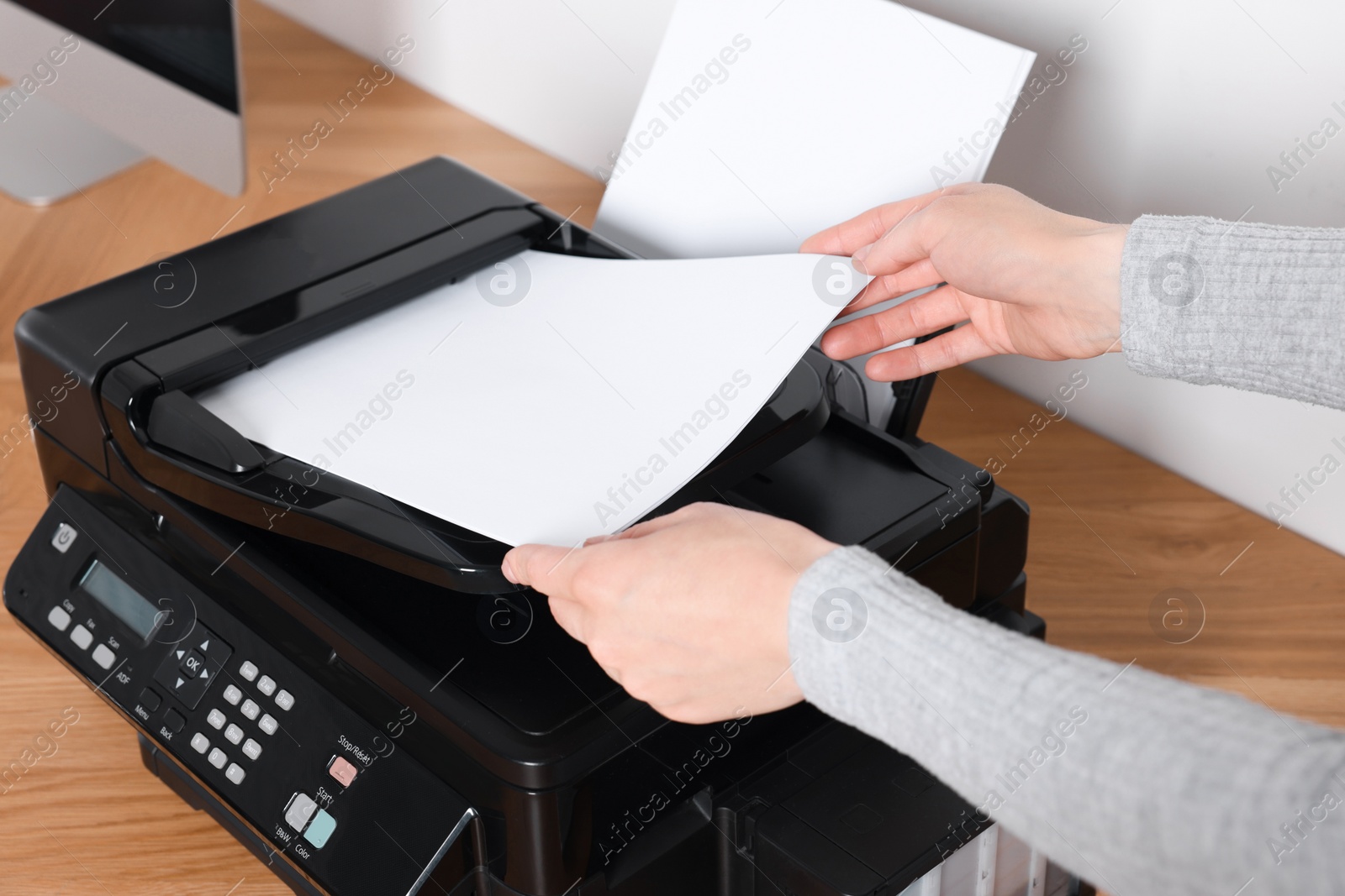 Photo of Woman loading paper into printer at wooden table indoors, closeup