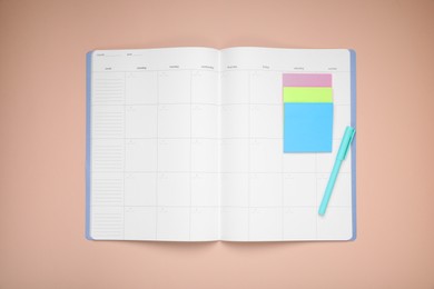 Photo of Open monthly planner, blank sticky notes and pen on beige background, top view. Space for text
