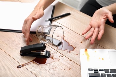 Photo of Woman spilled coffee on wooden office desk, closeup