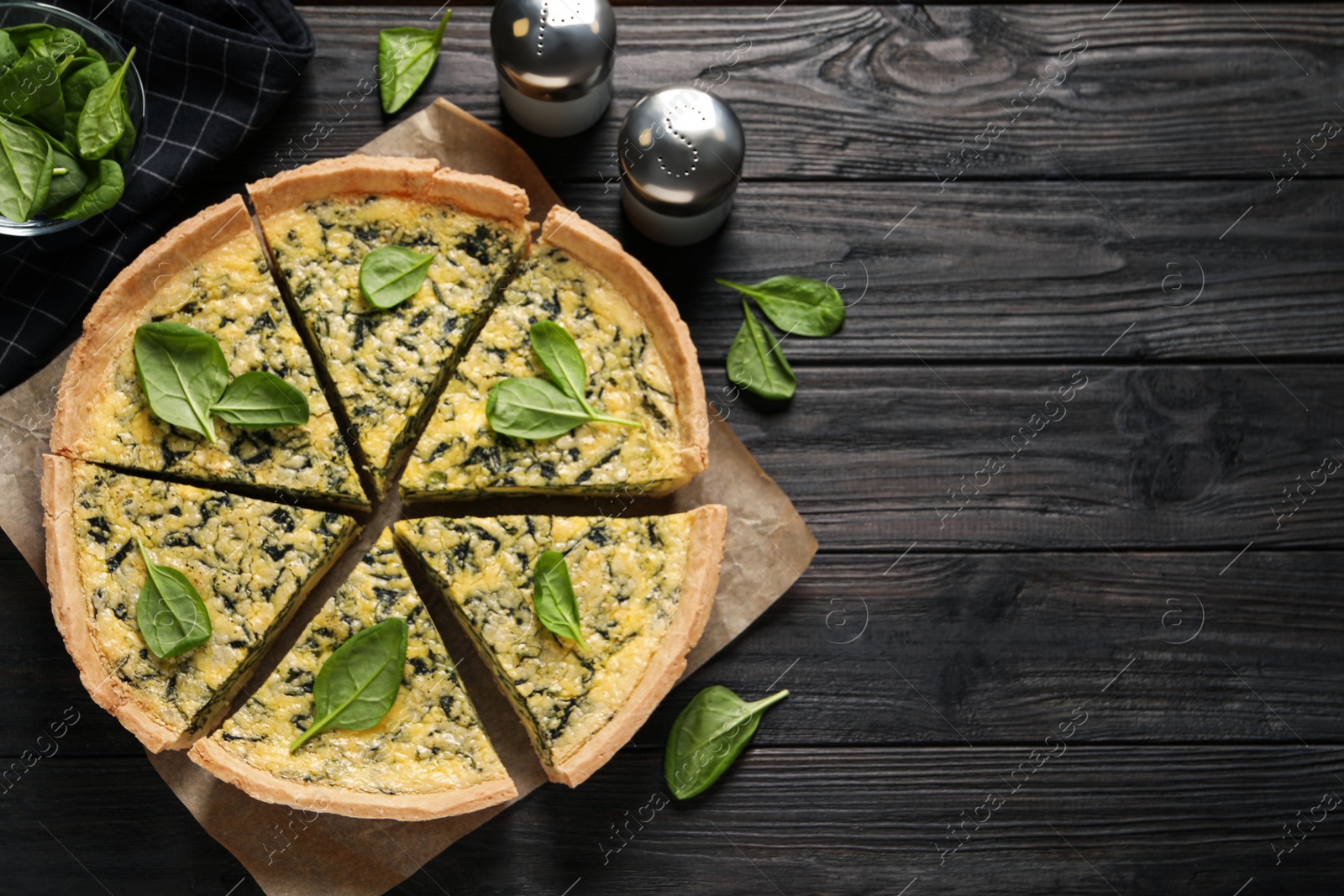 Photo of Sliced delicious homemade spinach pie on black wooden table, flat lay. Space for text