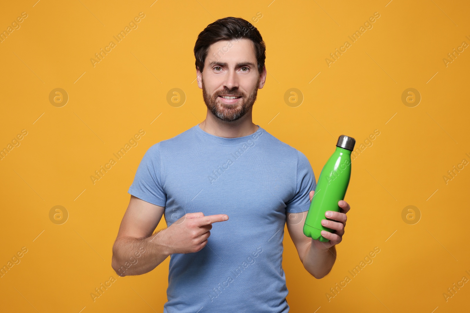 Photo of Man pointing at green thermo bottle on orange background