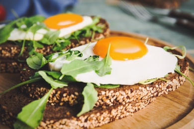 Delicious sandwiches with arugula and fried egg on wooden board, closeup