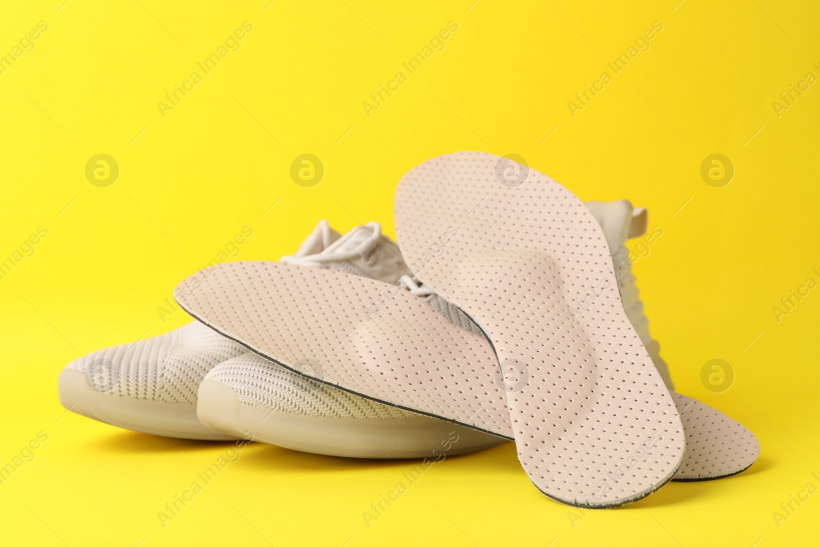 Photo of Beige orthopedic insoles and shoes on yellow background