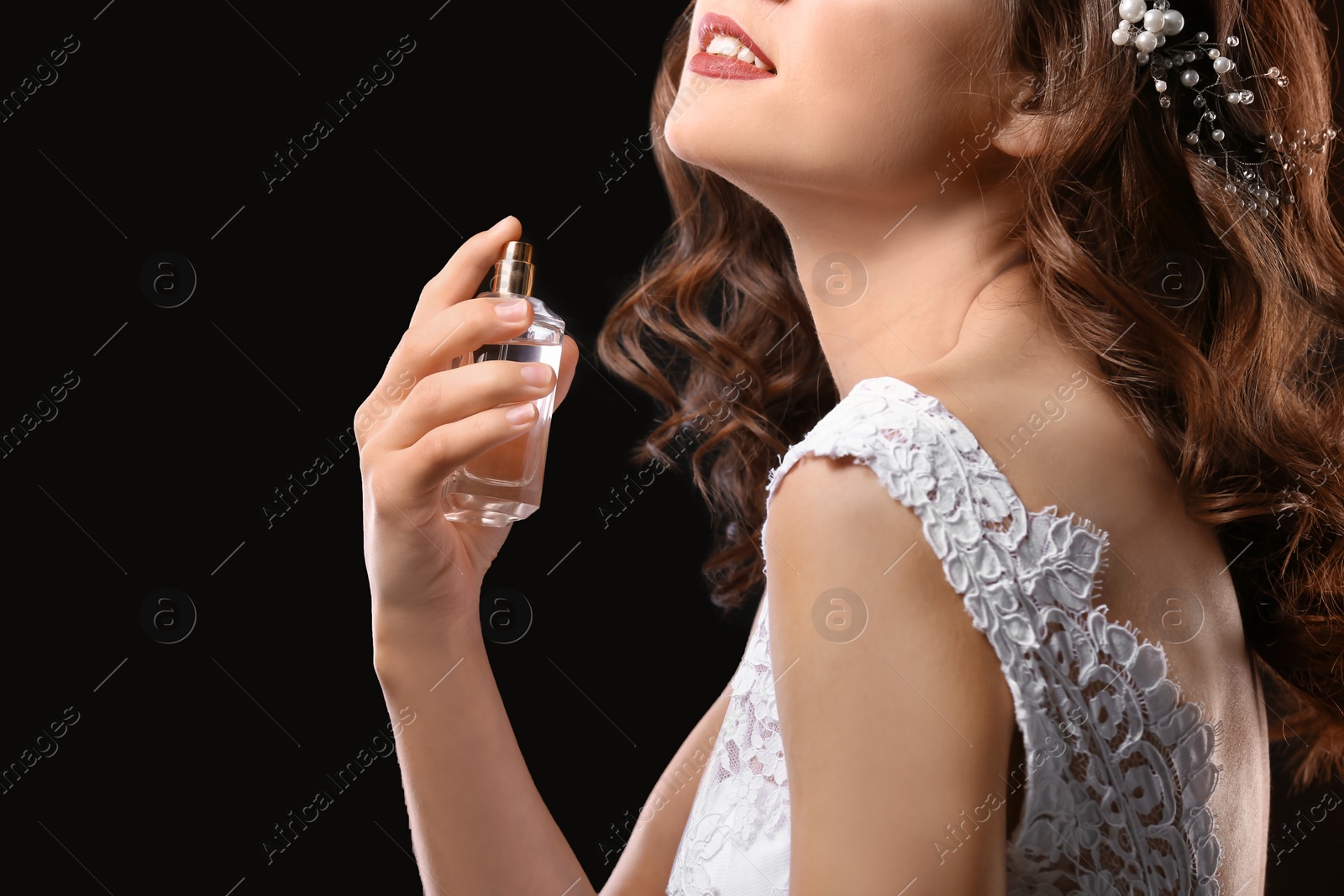 Photo of Beautiful young bride with bottle of perfume on black background, closeup