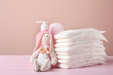Baby diapers, toy bunny and toiletries on wooden table against pink background