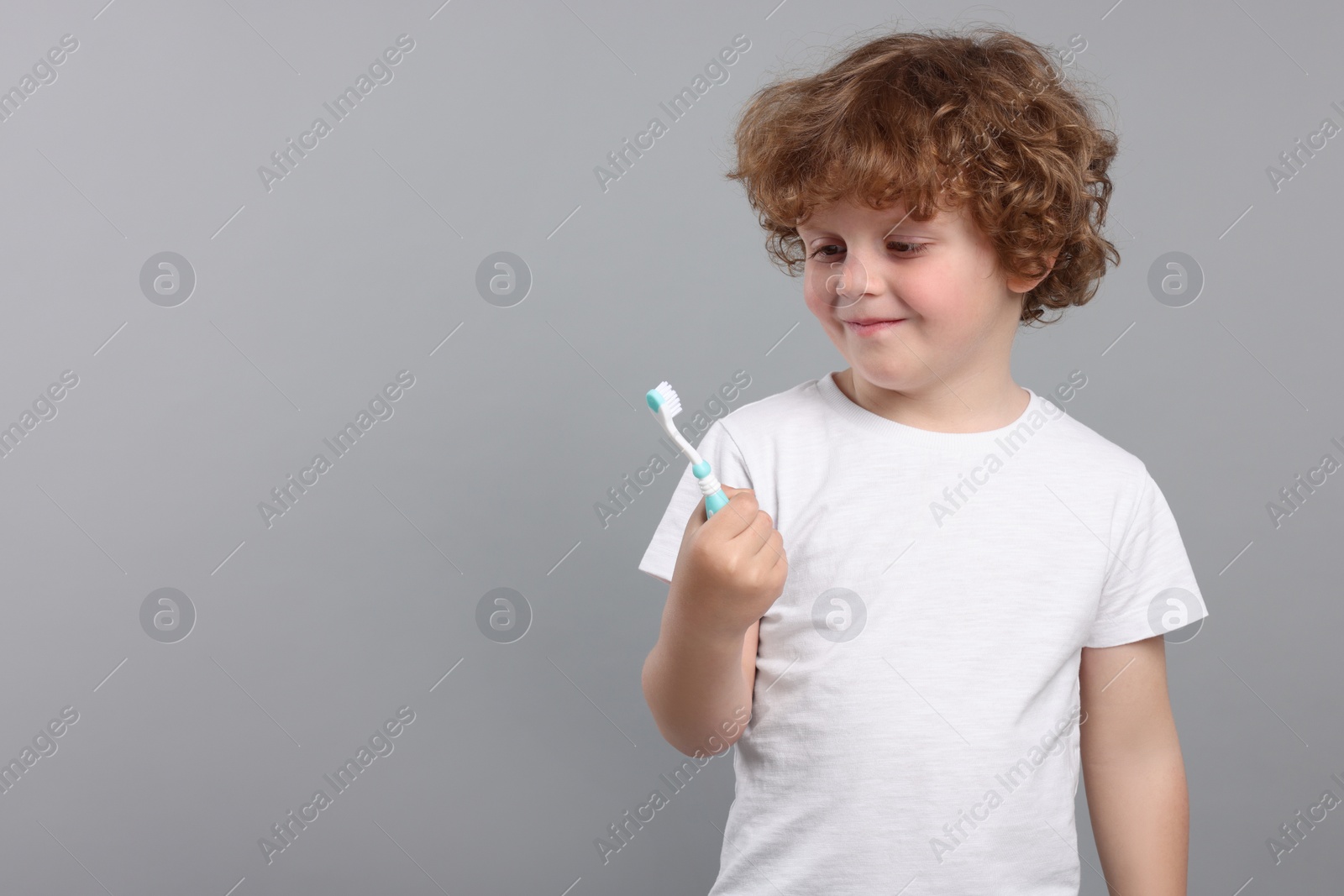 Photo of Cute little boy holding plastic toothbrush on light grey background, space for text