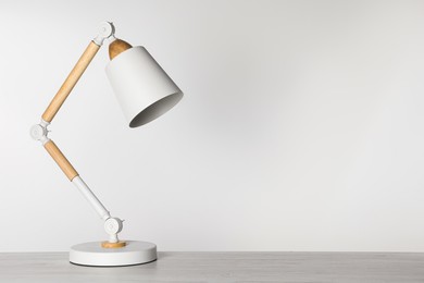 Photo of Stylish modern desk lamp on white wooden table, space for text