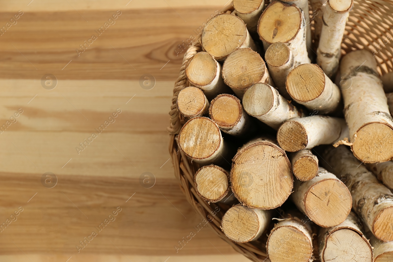 Photo of Wicker basket with firewood on floor indoors, top view. Space for text