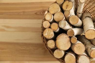 Wicker basket with firewood on floor indoors, top view. Space for text