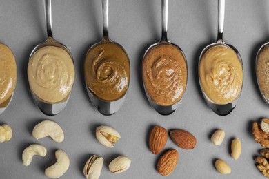 Photo of Tasty nut butters in spoons and raw nuts on gray table, flat lay