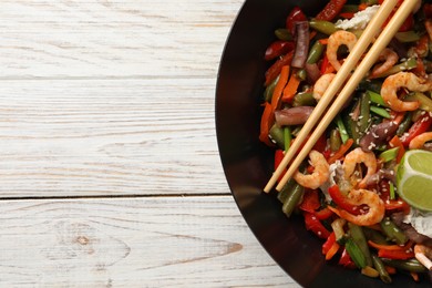 Photo of Shrimp stir fry with vegetables in wok and chopsticks on light wooden table, top view. Space for text