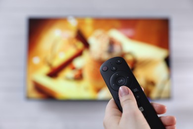Photo of Woman with remote control watching TV at home, closeup. Space for text