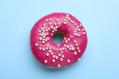 Tasty glazed donut decorated with sprinkles on light blue background, top view