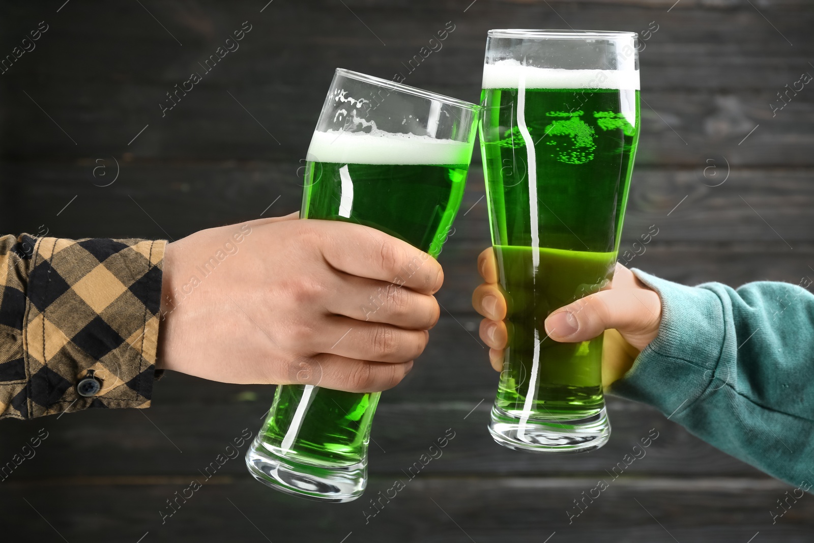 Photo of Man and woman toasting with green beer on black wooden background, closeup. St. Patrick's Day celebration