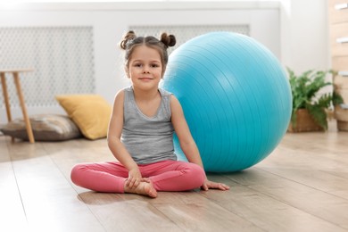 Little cute girl with fitness ball on floor at home. Doing exercises