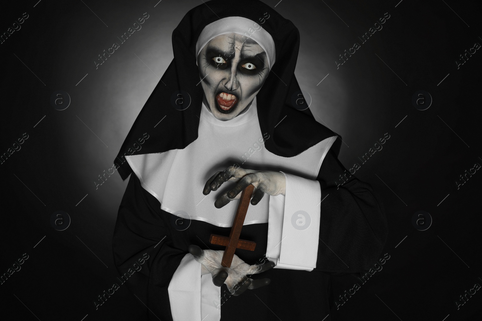 Photo of Scary devilish nun with cross on black background. Halloween party look