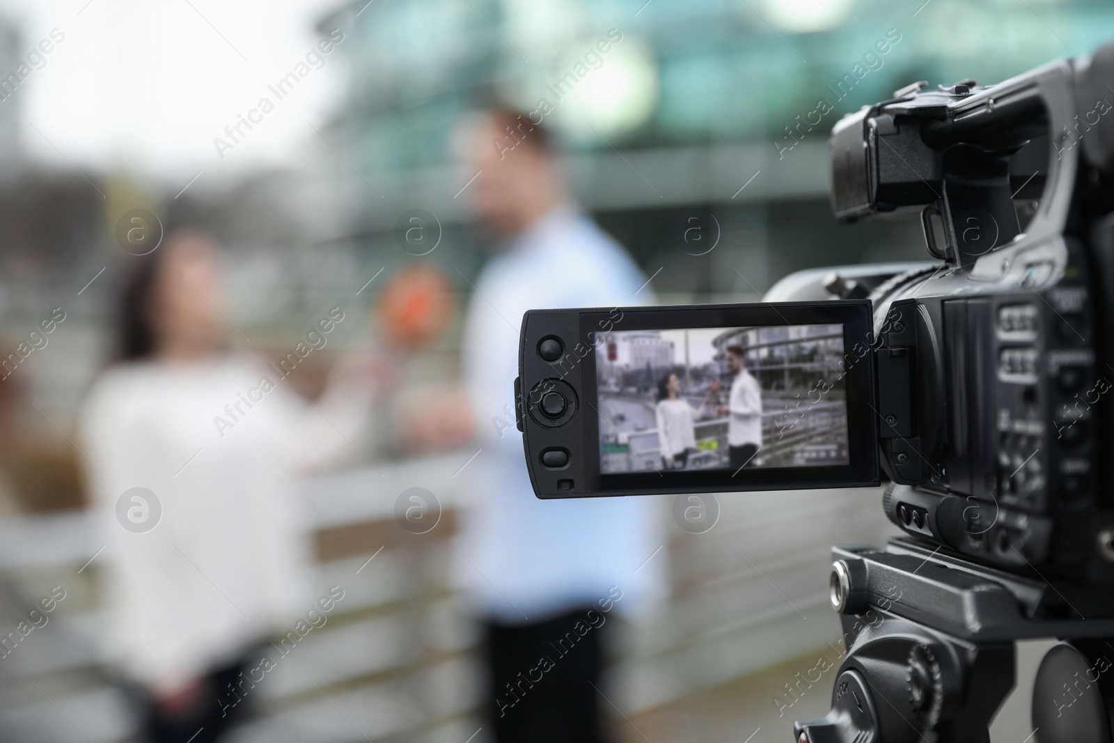 Photo of Young journalist interviewing man on city street, focus on camera display. Space for text